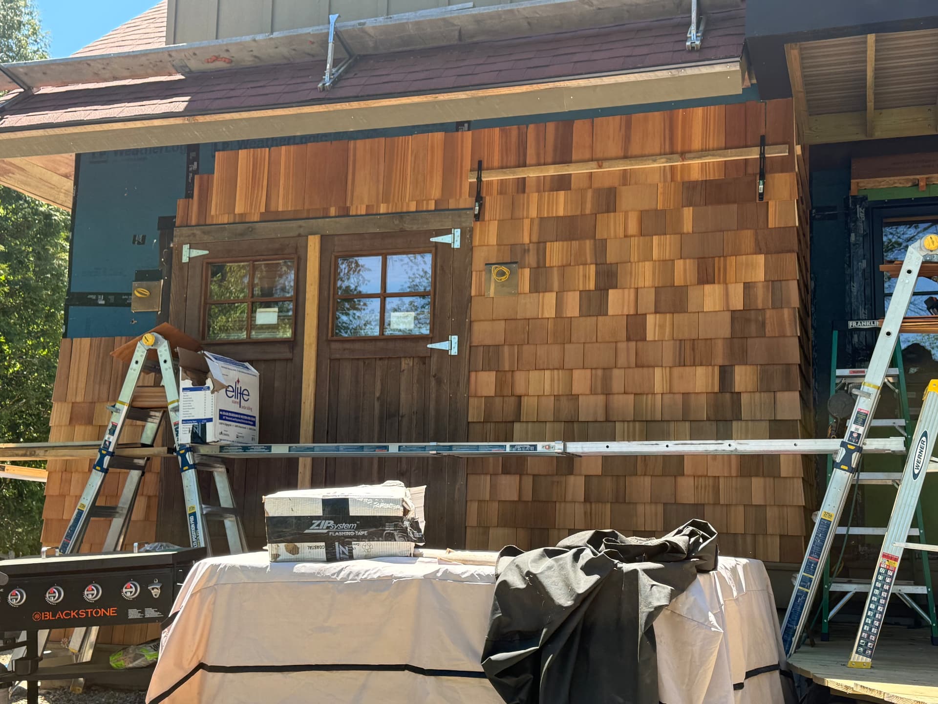 Cedar shake siding installation in progress around barn style doors